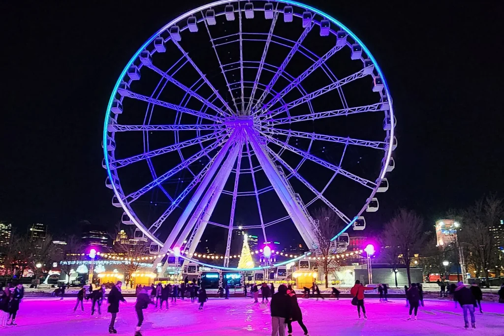 People ice skating in the old port of montreal in front of the ferris wheel