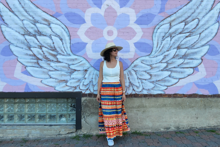 a girl standing in front of a mural depicting wings